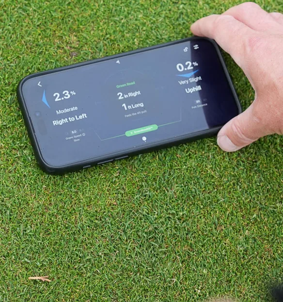 A phone lying on the green reading the slope between ball and hole